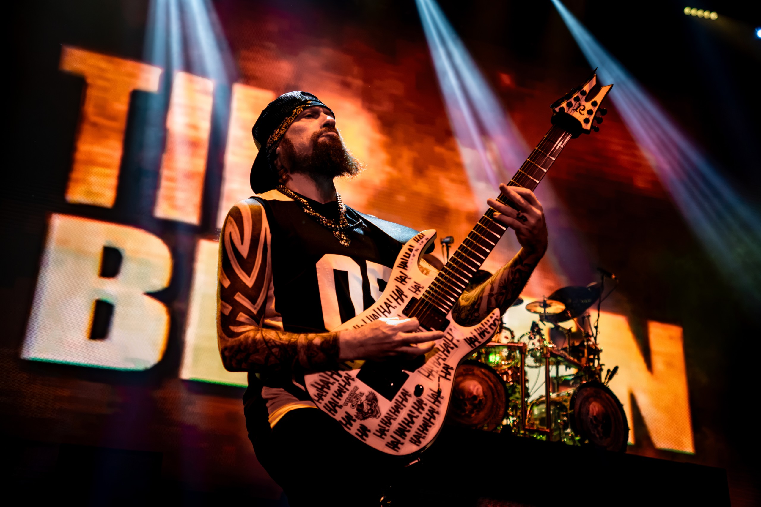 Five Finger Death Punch guitarist performing beneath orange and blue stage lights. Five Finger Death Punch at Coastal Credit Union Music Park, Raleigh, October 14, 2026.