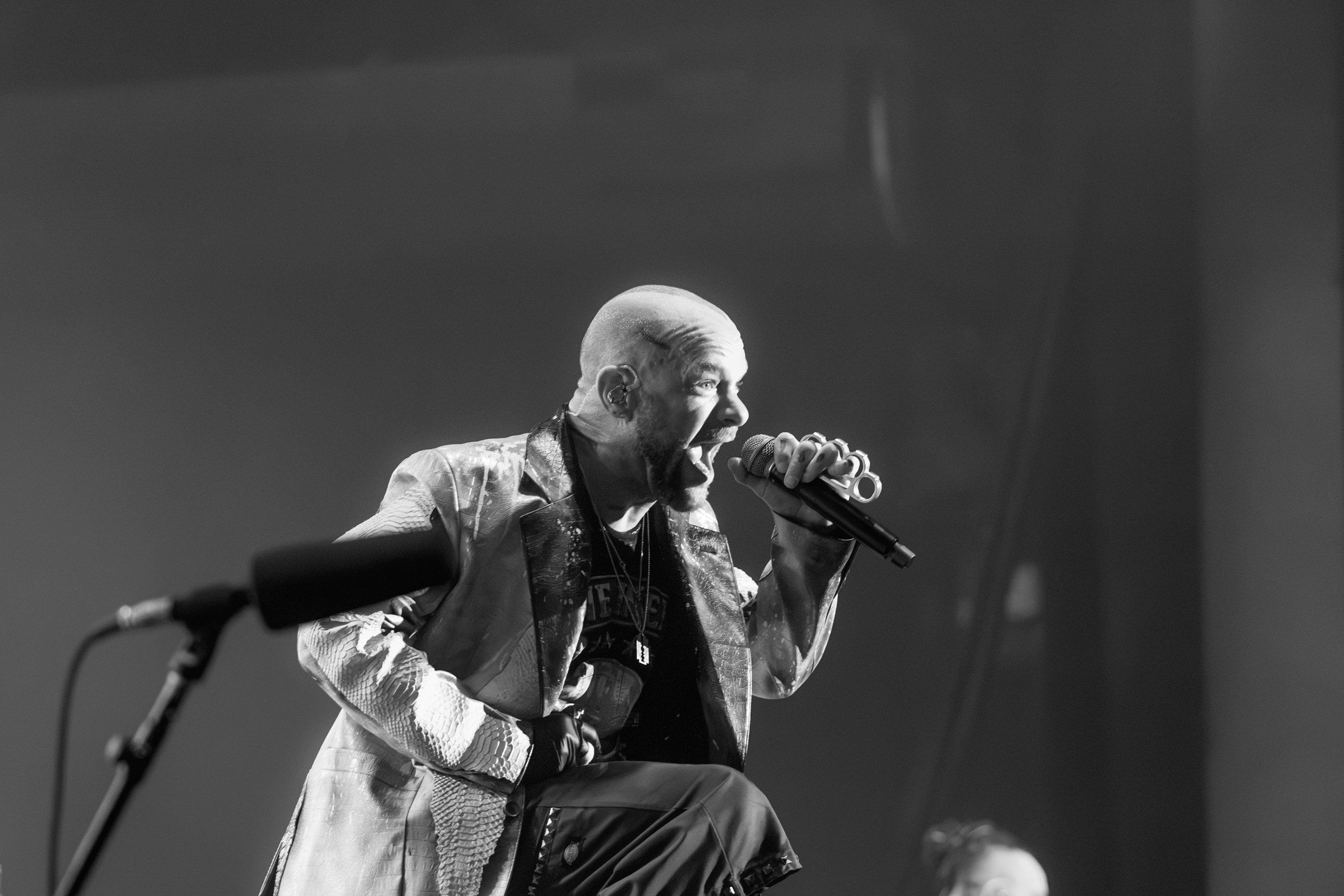 Black-and-white photograph of Ivan Moody leaning toward a microphone. Five Finger Death Punch at Coastal Credit Union Music Park, Raleigh, October 14, 2026.