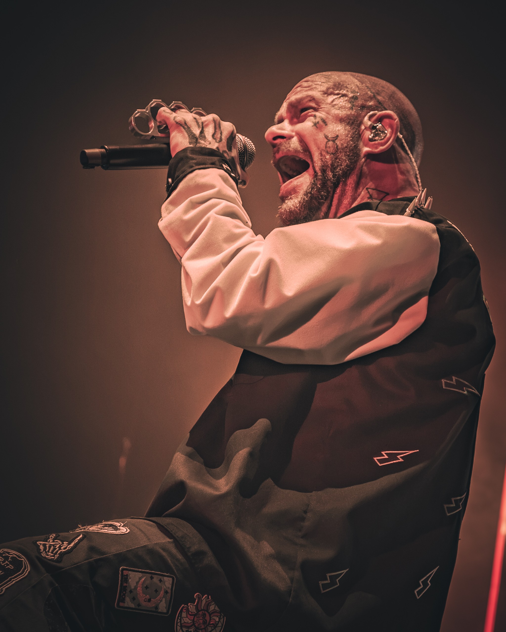 Ivan Moody singing in profile beneath soft stage lighting. Five Finger Death Punch at Coastal Credit Union Music Park, Raleigh, October 14, 2026.