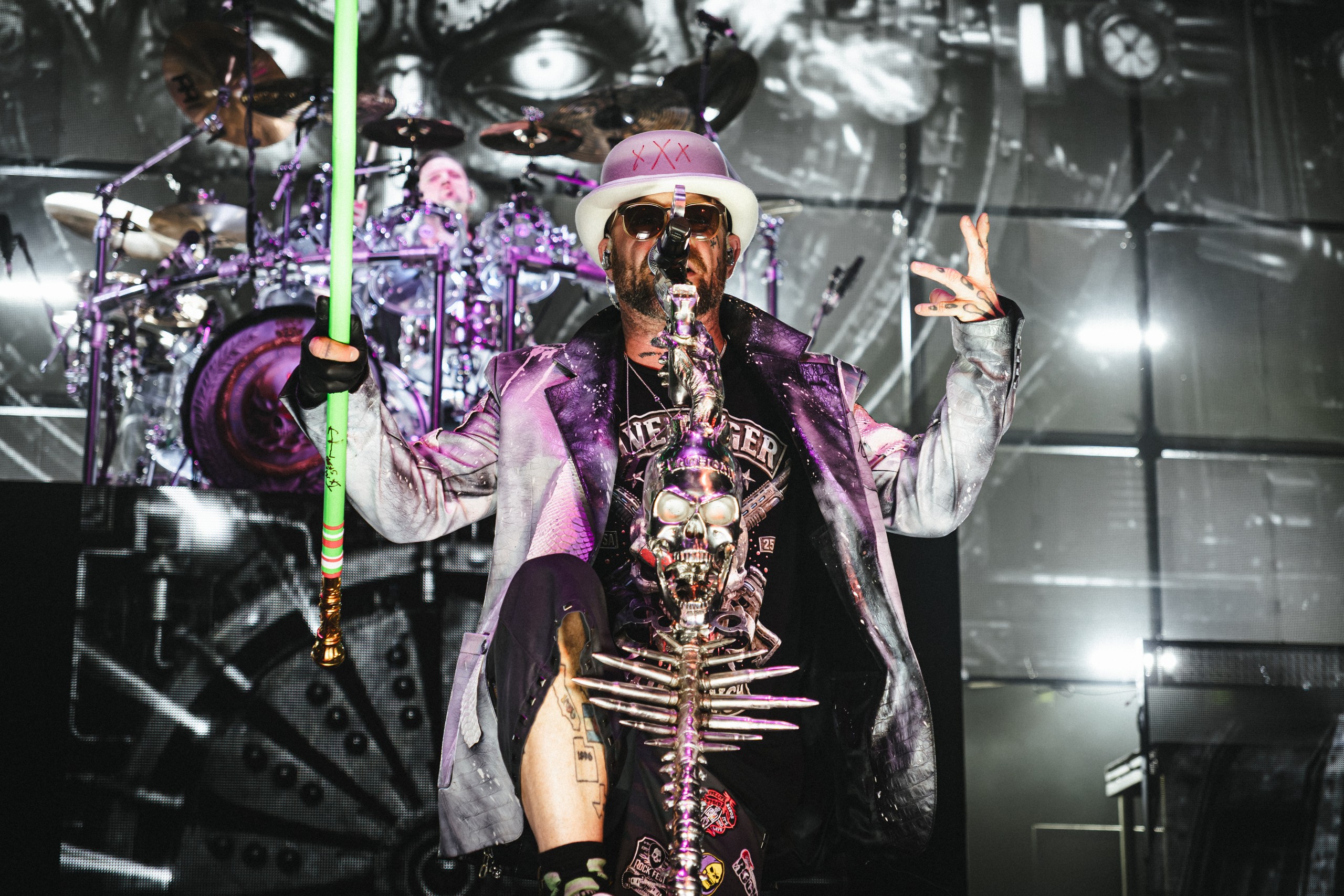 Ivan Moody in a hat and sunglasses, raising his hands beside the microphone stand. Five Finger Death Punch at Coastal Credit Union Music Park, Raleigh, October 14, 2026.