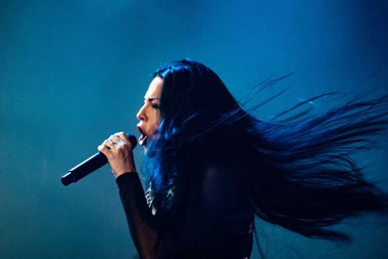 Amy Lee singing into a microphone as her hair sweeps across blue stage light.