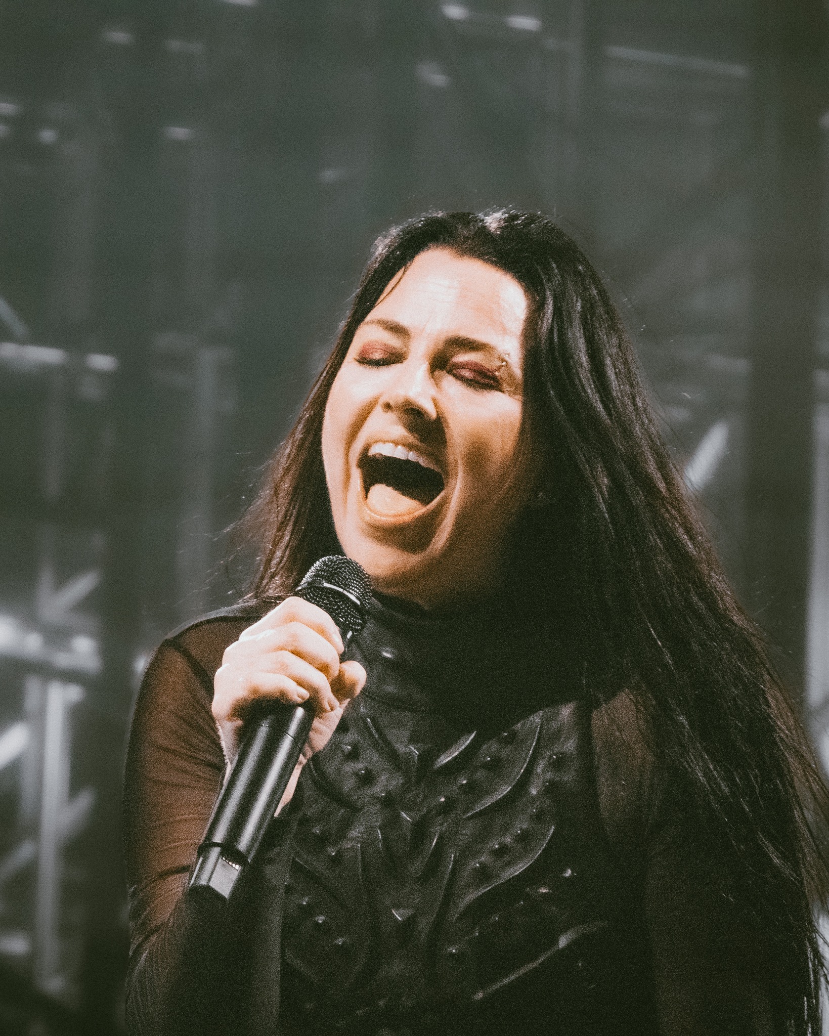 Amy Lee smiling at the microphone under white light.