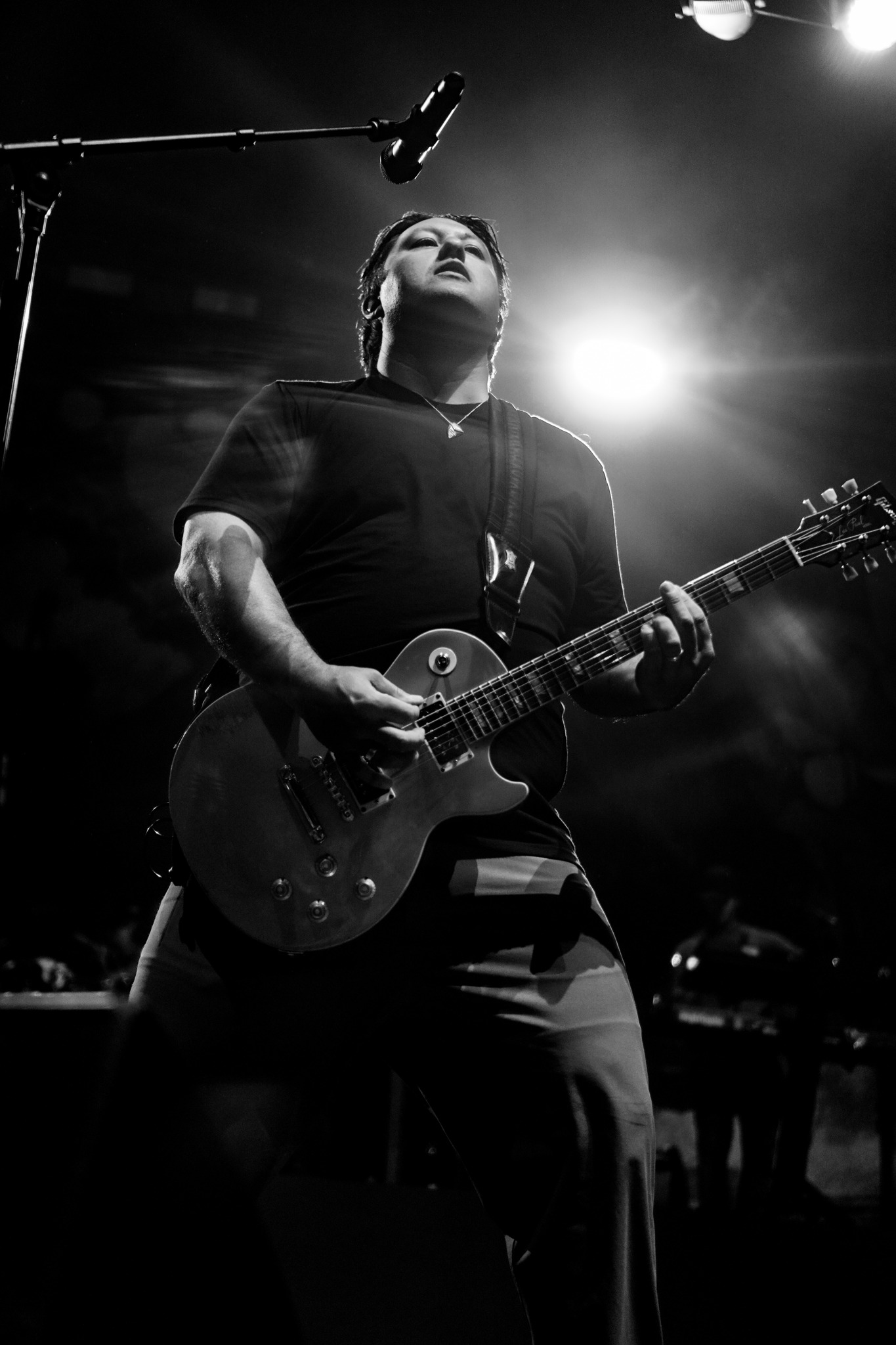 Black and white photograph of an Iration guitarist beneath stage lights.