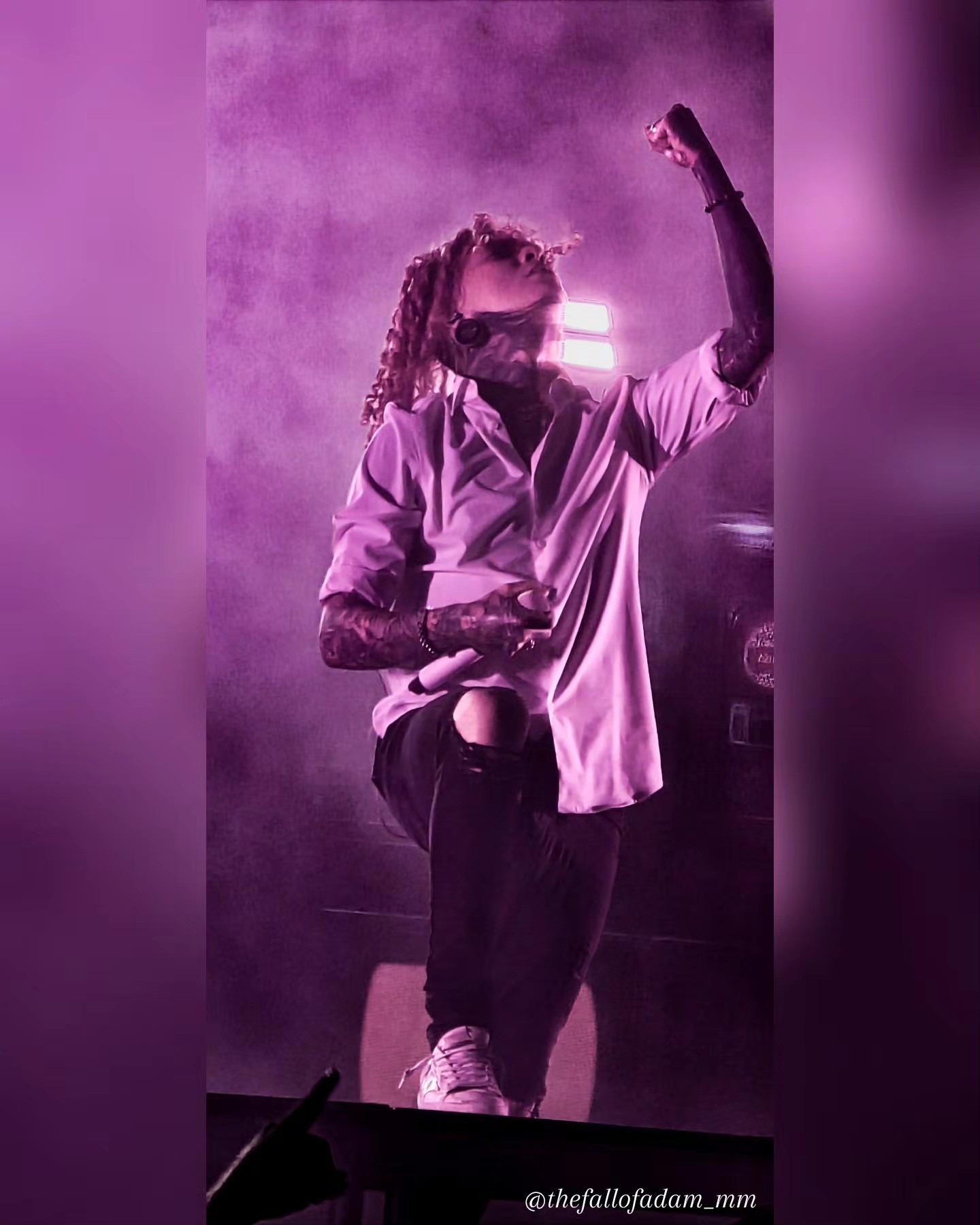 Lorna Shore vocalist raising a hand under pink stage light.