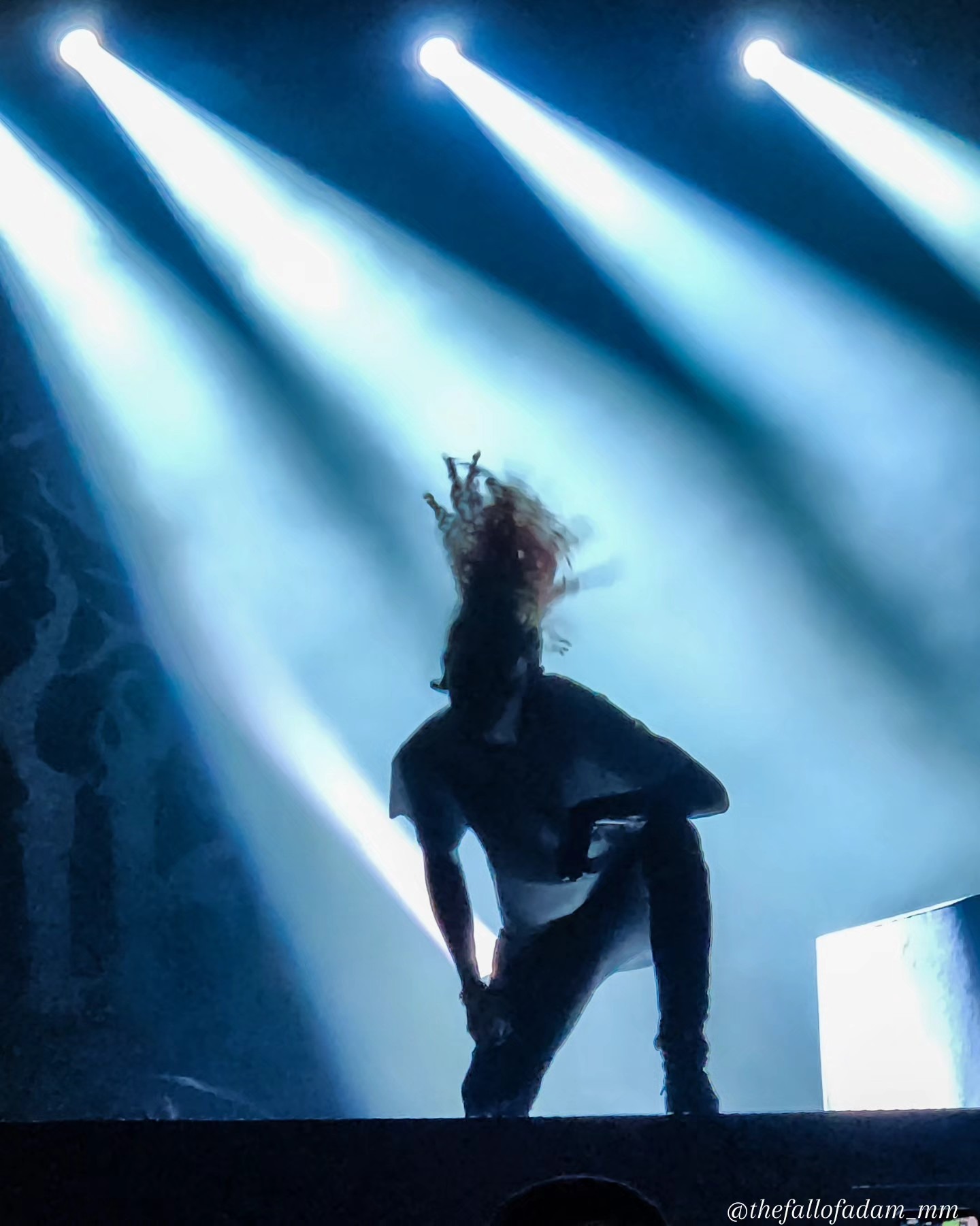 Lorna Shore vocalist silhouetted beneath bright blue stage beams.