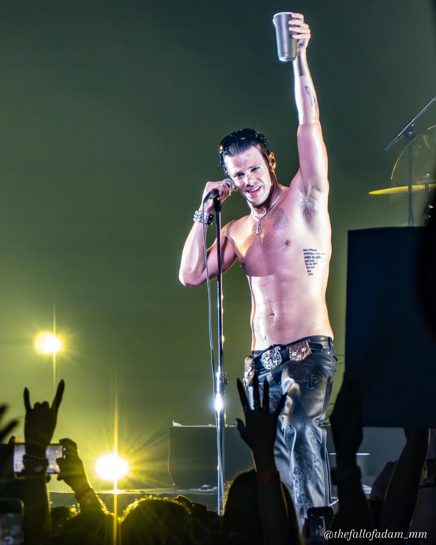 Yungblud raising the microphone toward the crowd under gold light.