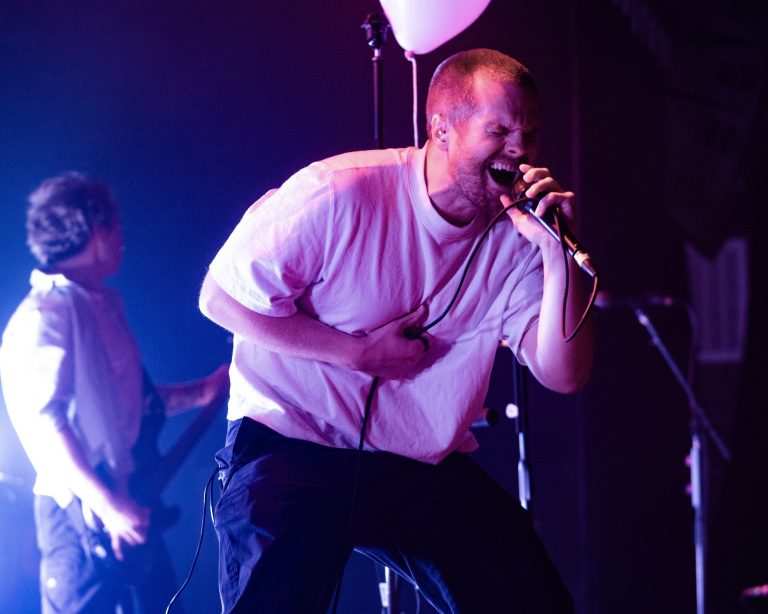 Dead Poet Society vocalist leaning toward the crowd under purple lights.