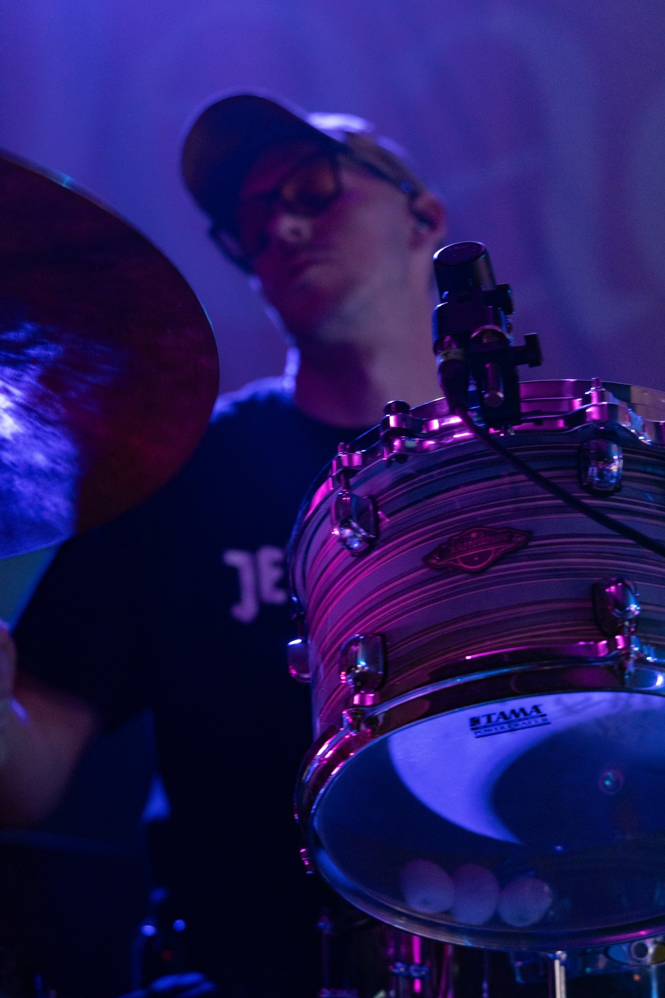 Dead Poet Society drummer at his kit under purple lights.