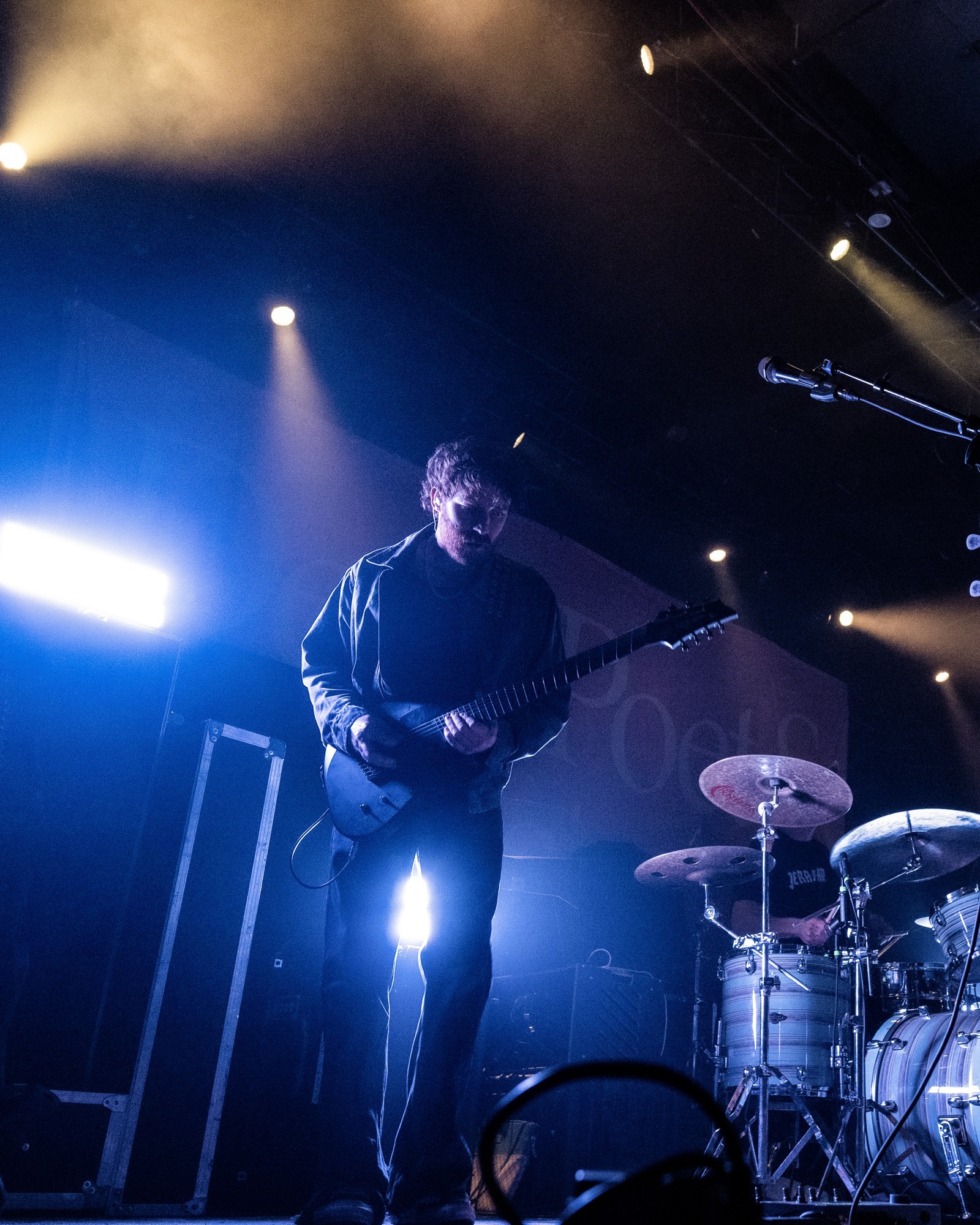 Dead Poet Society bassist performing beneath blue and gold lights.