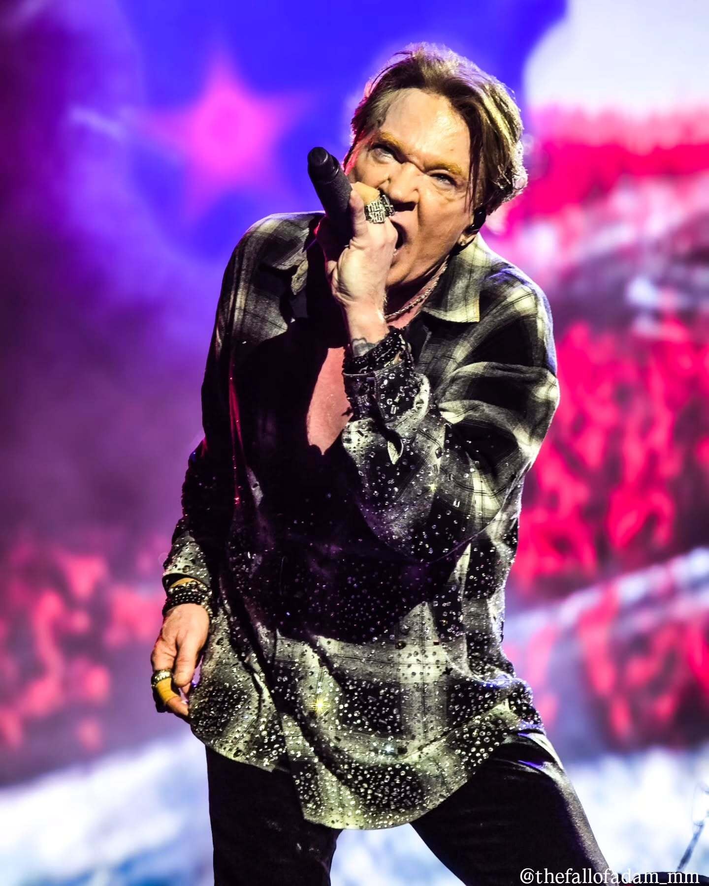 Axl Rose singing against a vivid pink stage backdrop.