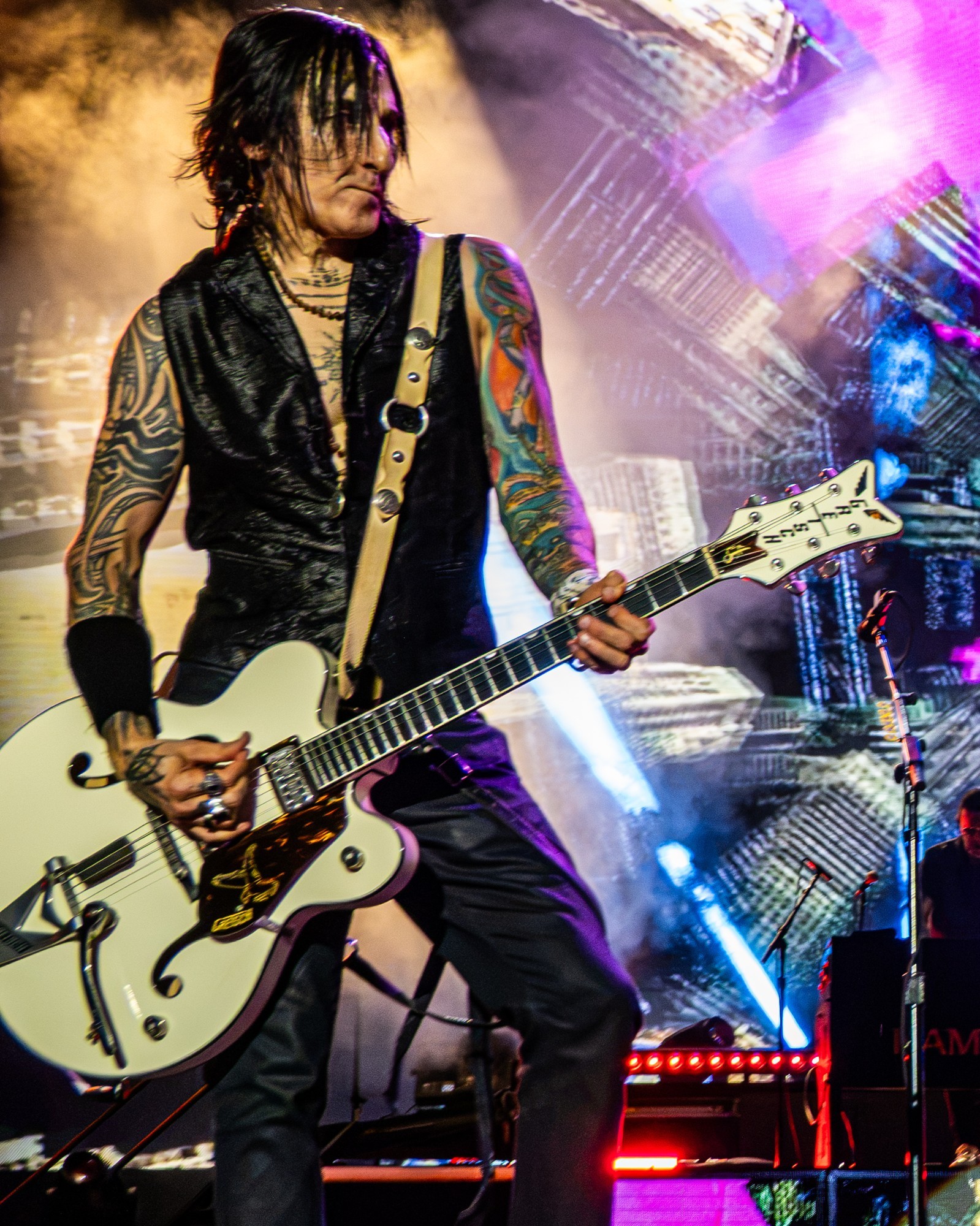 Richard Fortus performing beneath gold and purple lights.