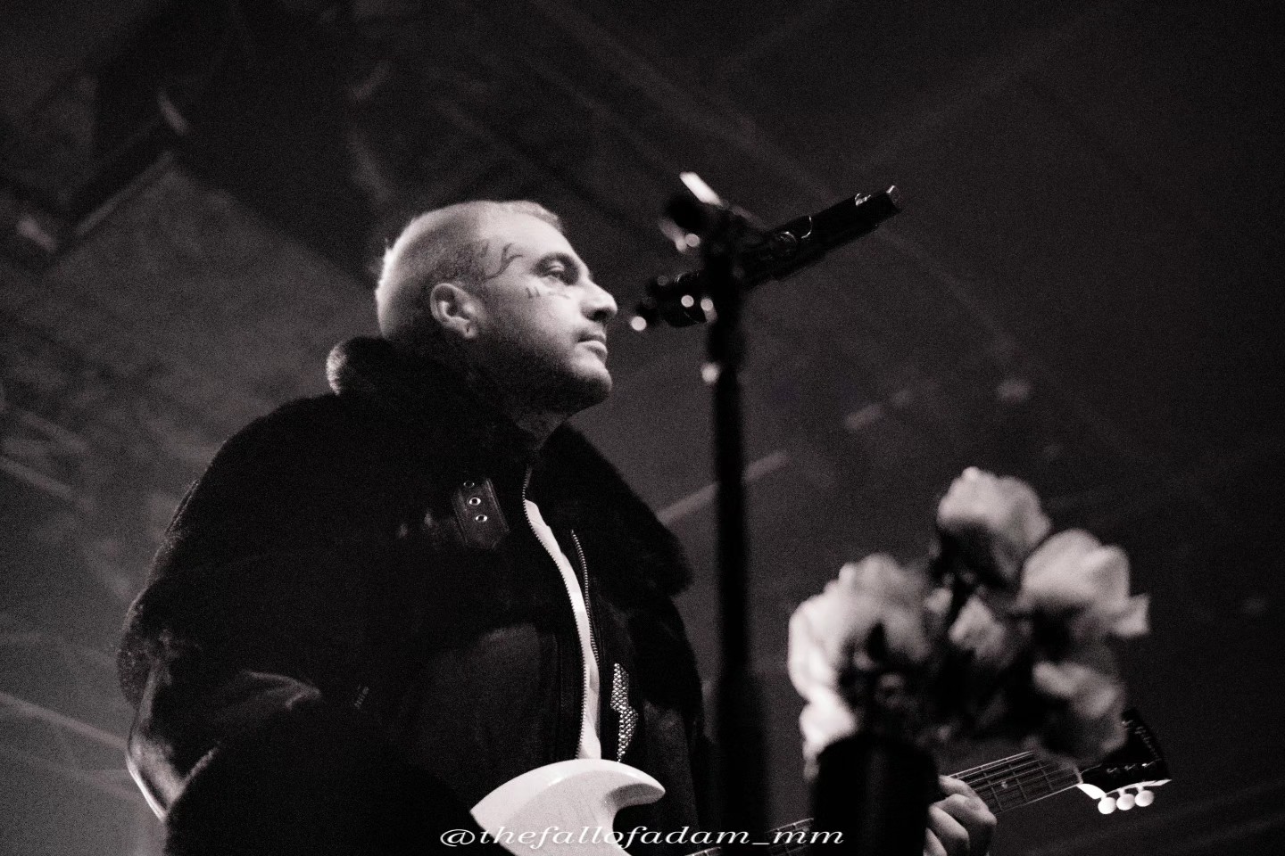 Black and white photograph of the Highly Suspect vocalist playing guitar beside stage flowers.