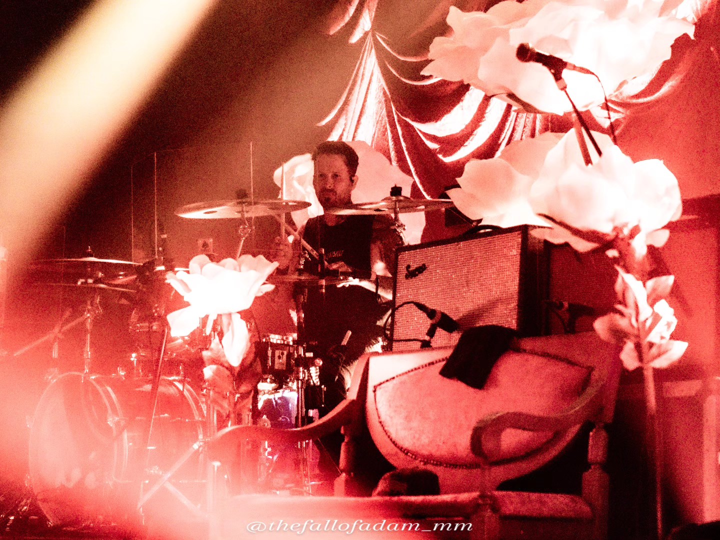 Highly Suspect drummer surrounded by large flower decorations and warm stage lights.