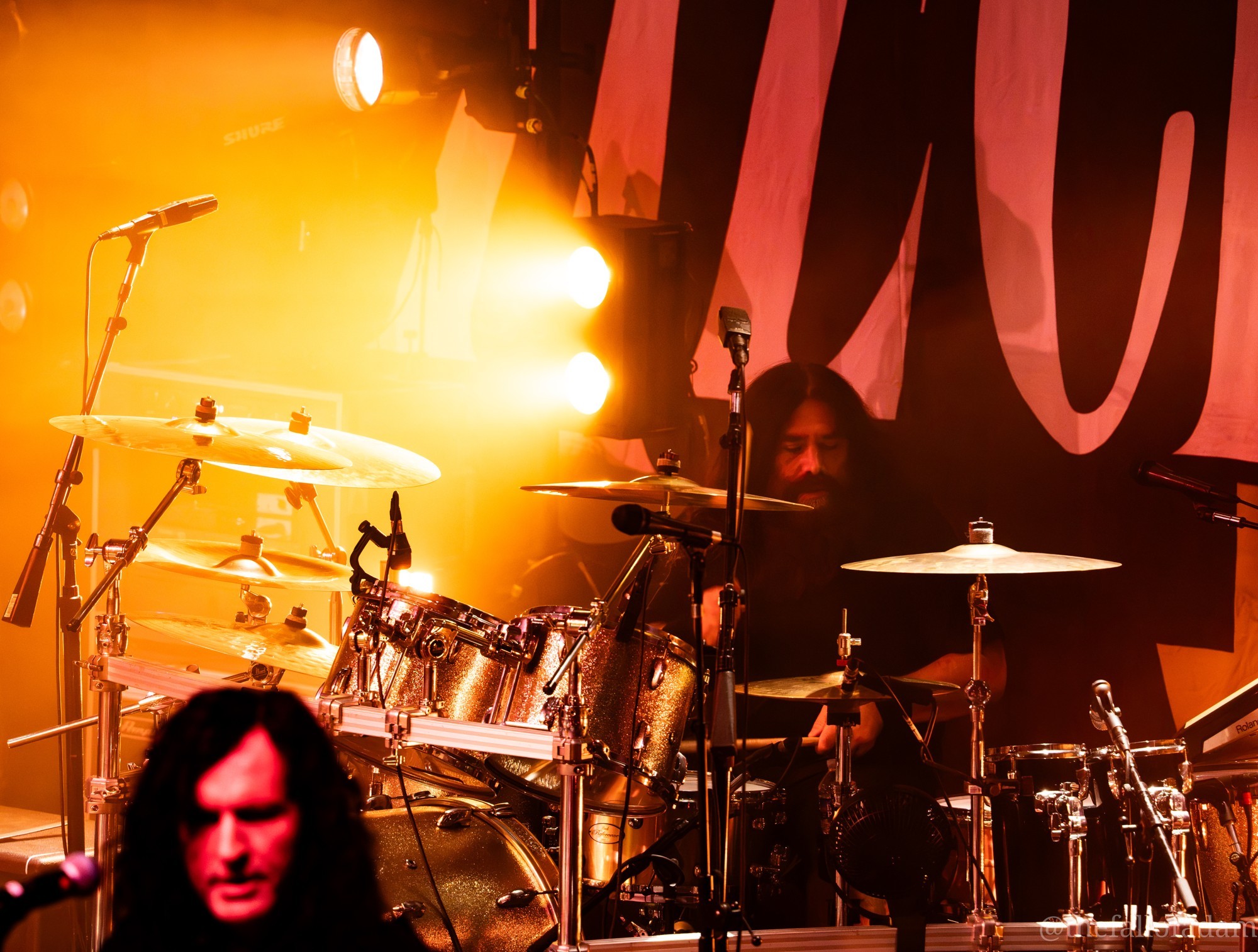 The Pretty Reckless drummer behind his kit beneath amber lights.