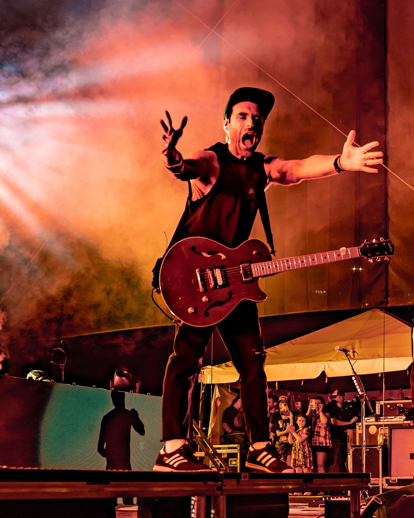Simple Plan guitarist reaching toward the crowd amid red stage smoke.