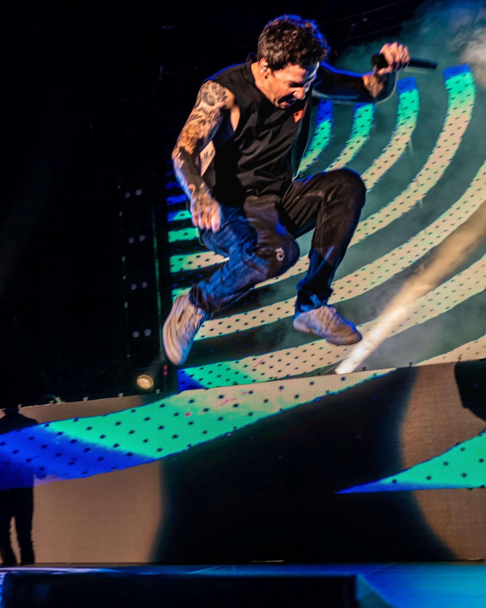 Simple Plan vocalist crouching in front of a colorful stage backdrop.