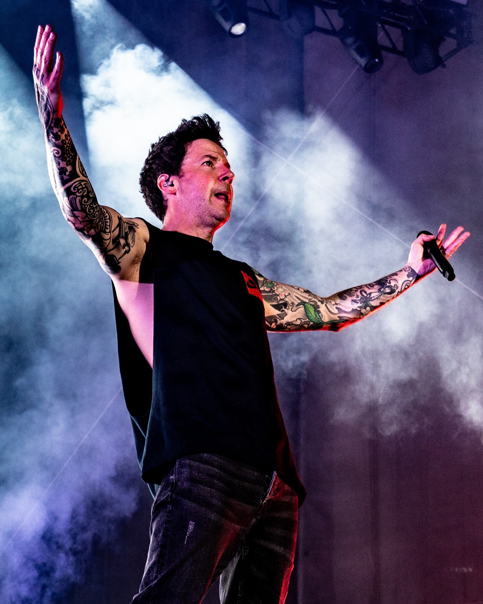 Simple Plan vocalist spreading his arms amid stage smoke.